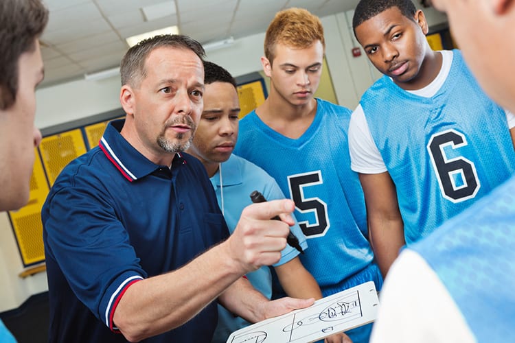 High school coach instructing basketball players in locker room