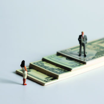 A miniature man and a miniature woman standing on a pile of bills.