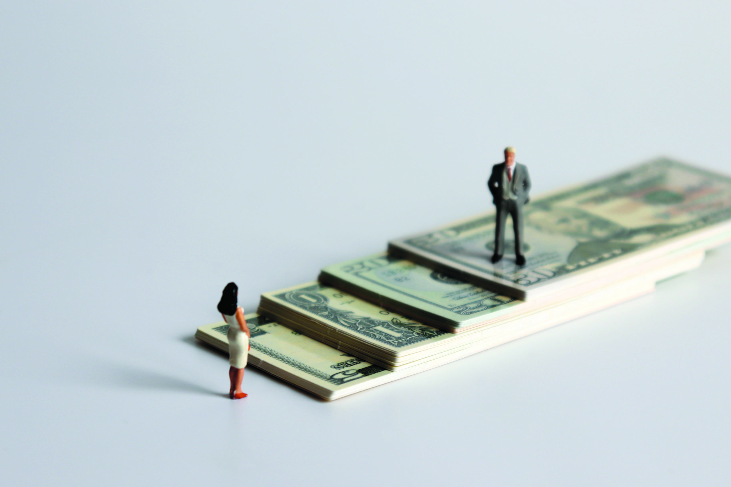 A miniature man and a miniature woman standing on a pile of bills.