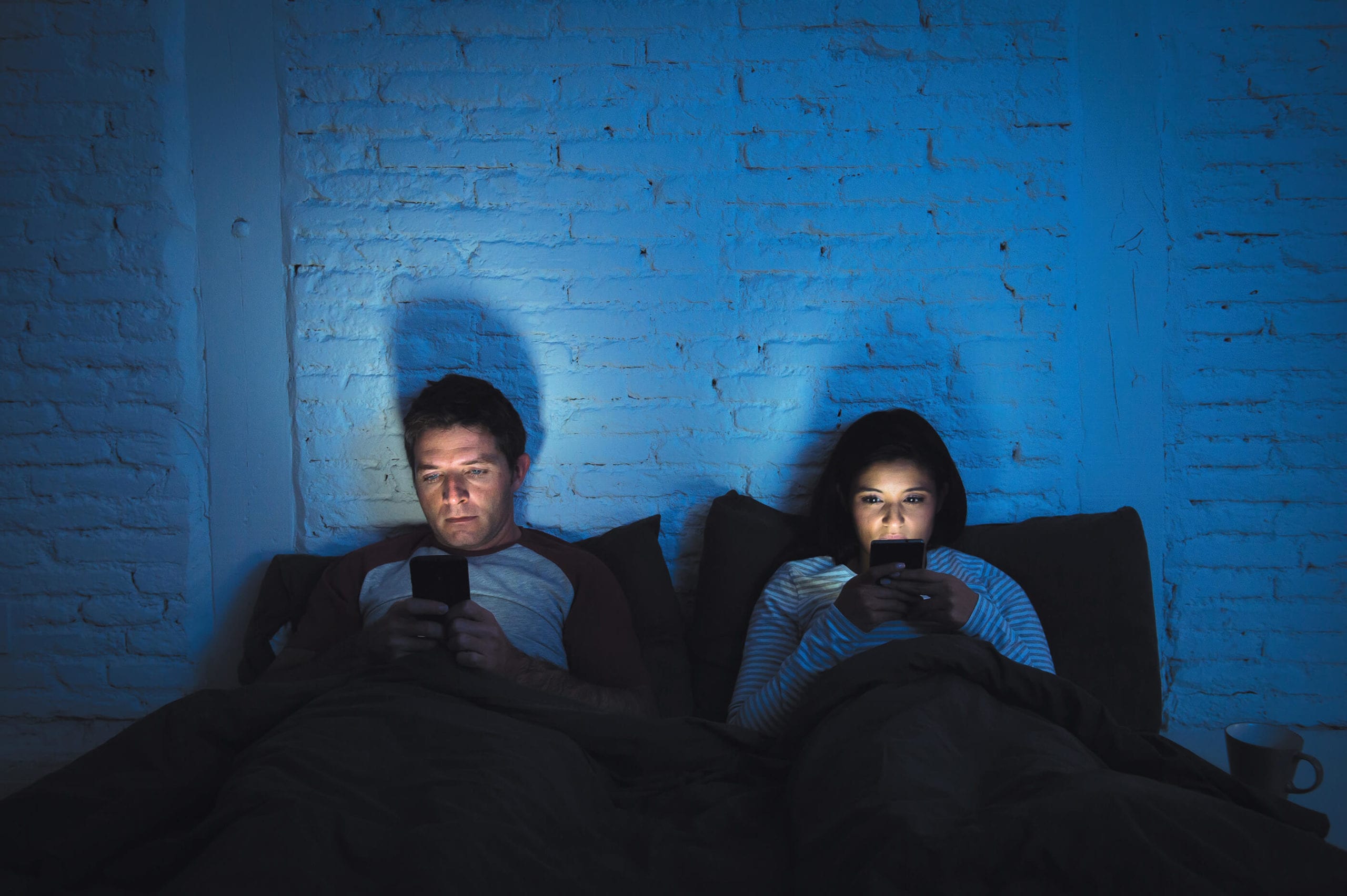 Two people sitting in bed engrossed in their own mobile device.