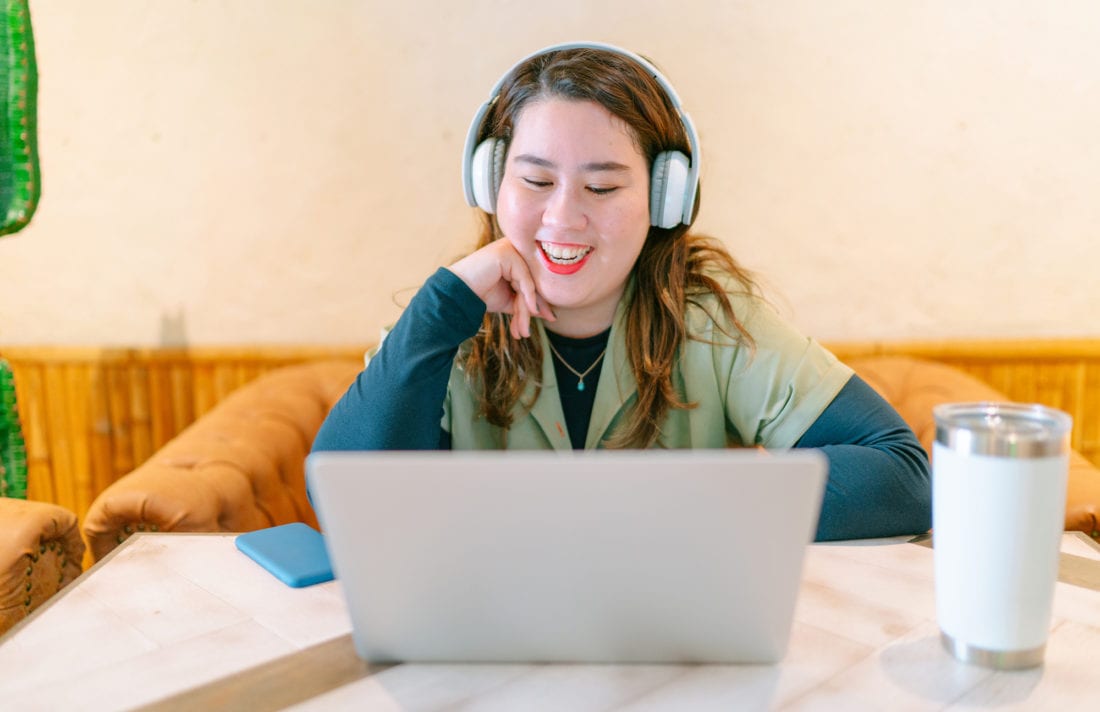 A smiling woman in headphones works at her laptop