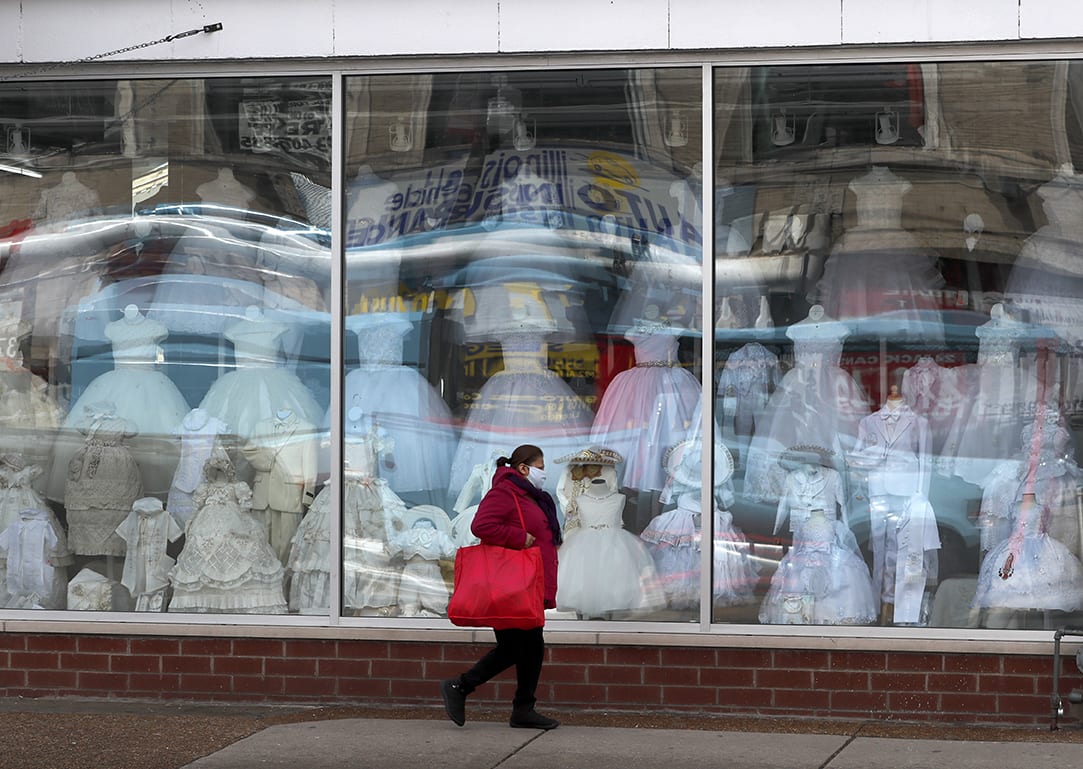A woman wearing a protective mask walks past a closed children's clothing store in Chicago, Wednesday, April 15, 2020. (AP Photo/Charles Rex Arbogast)