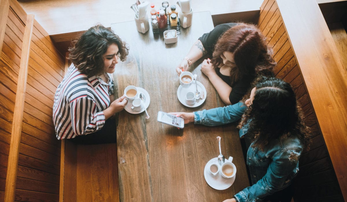Three women taking over lattes at a cafe.