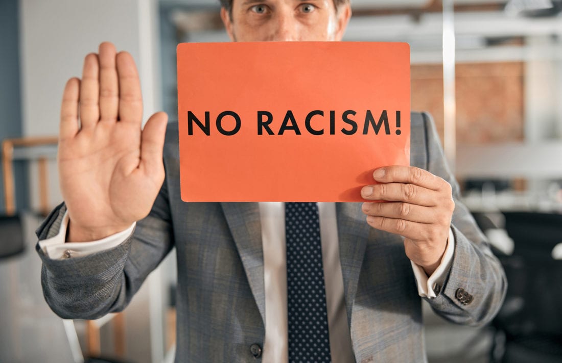 Close up of white man in suit holding a poster that says "no racism"
