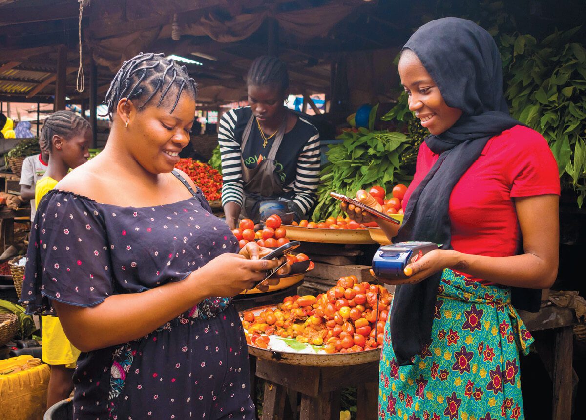 A woman using a mobile device to pay for a purchase at a produce stand from another woman.
