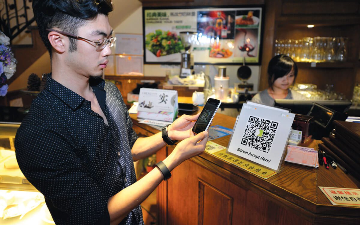 Man scanning a QR code on a sign reading "Bitcoin accepted here."