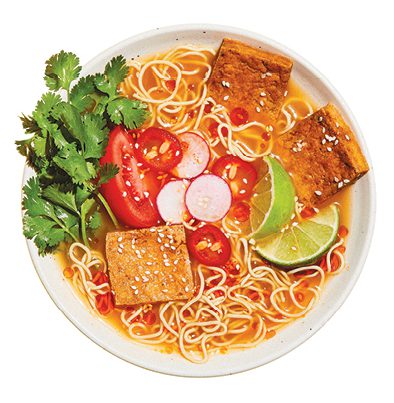 A bowl of ramen with tofu, radishes, tomatoes, limes, and cilantro created using immi noodles and broth.