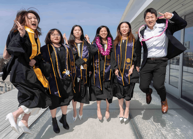 Six graduates donned in academic regalia jump in the air