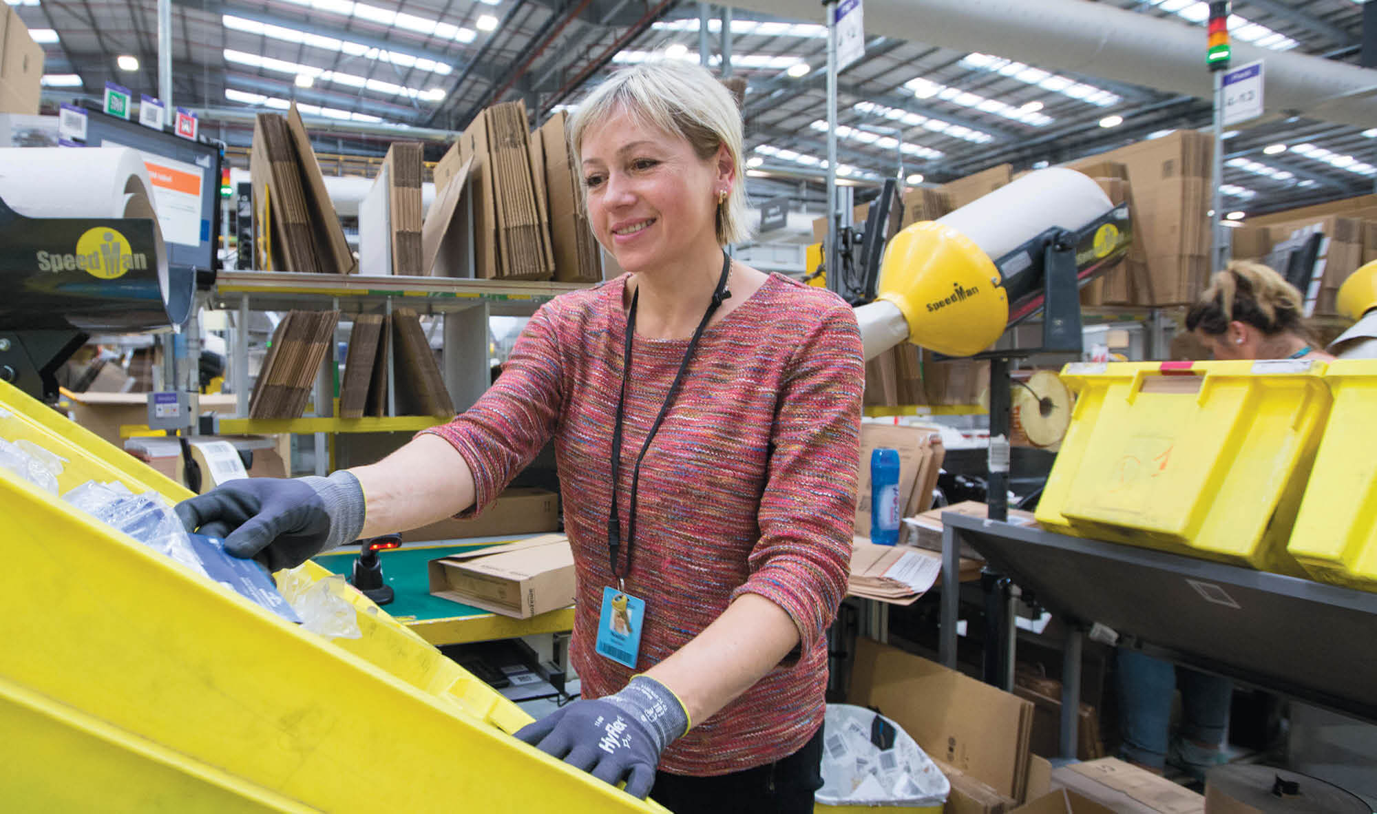 A woman sorting through items in a yellow bin at an Amazon warehouse.