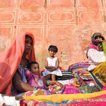 Two women street vendors selling colorful cloths and saris in Jaipur, India. Two small children are with them.