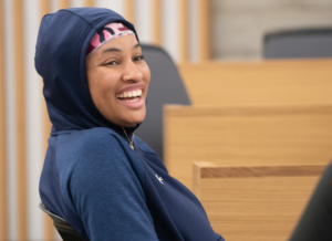 Black undergraduate student wearing blue hoodie smiles.