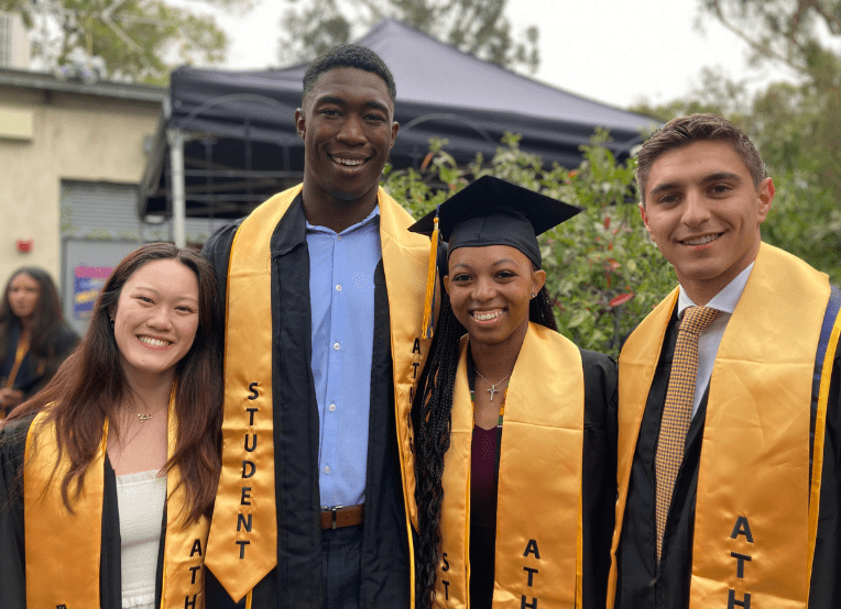Two women and two male student athletes dressed in academic regalia.