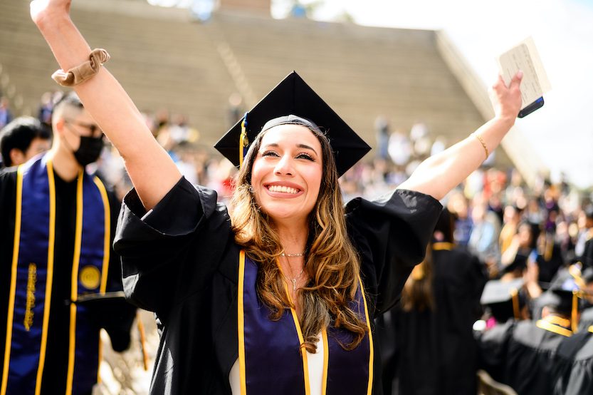 undergraduate woman in cap and gown cheering 