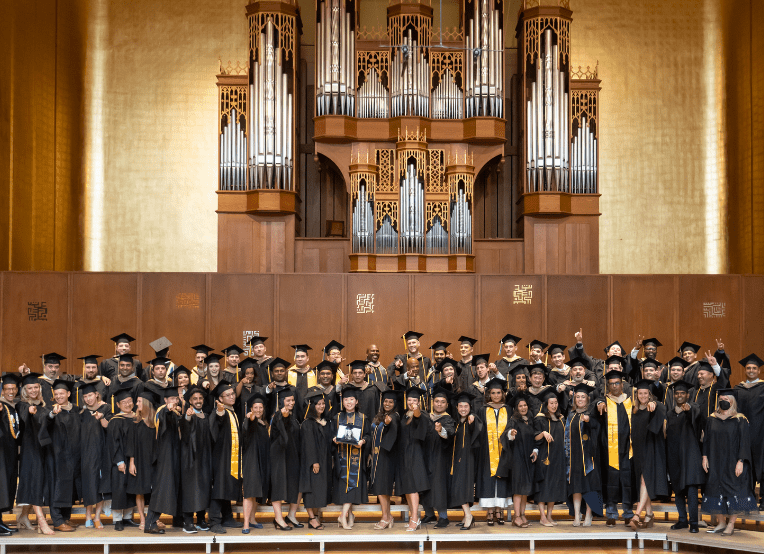 64 graduates dressed in caps and gowns