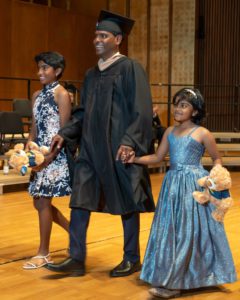 Male graduate crosses stage with his two young daughters