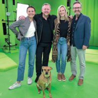 Four people and a dog standing against a green screen.