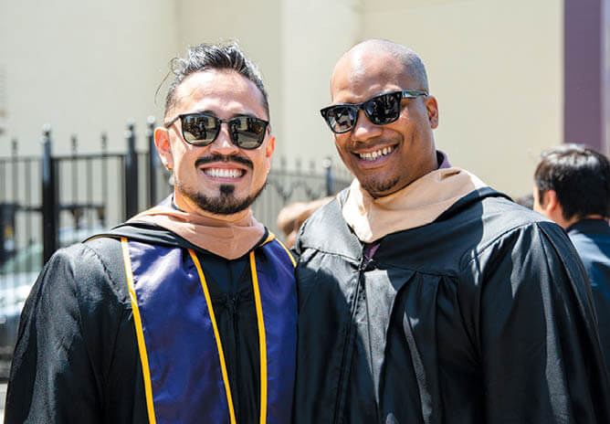 Two men in graduation gowns standing next to one another.