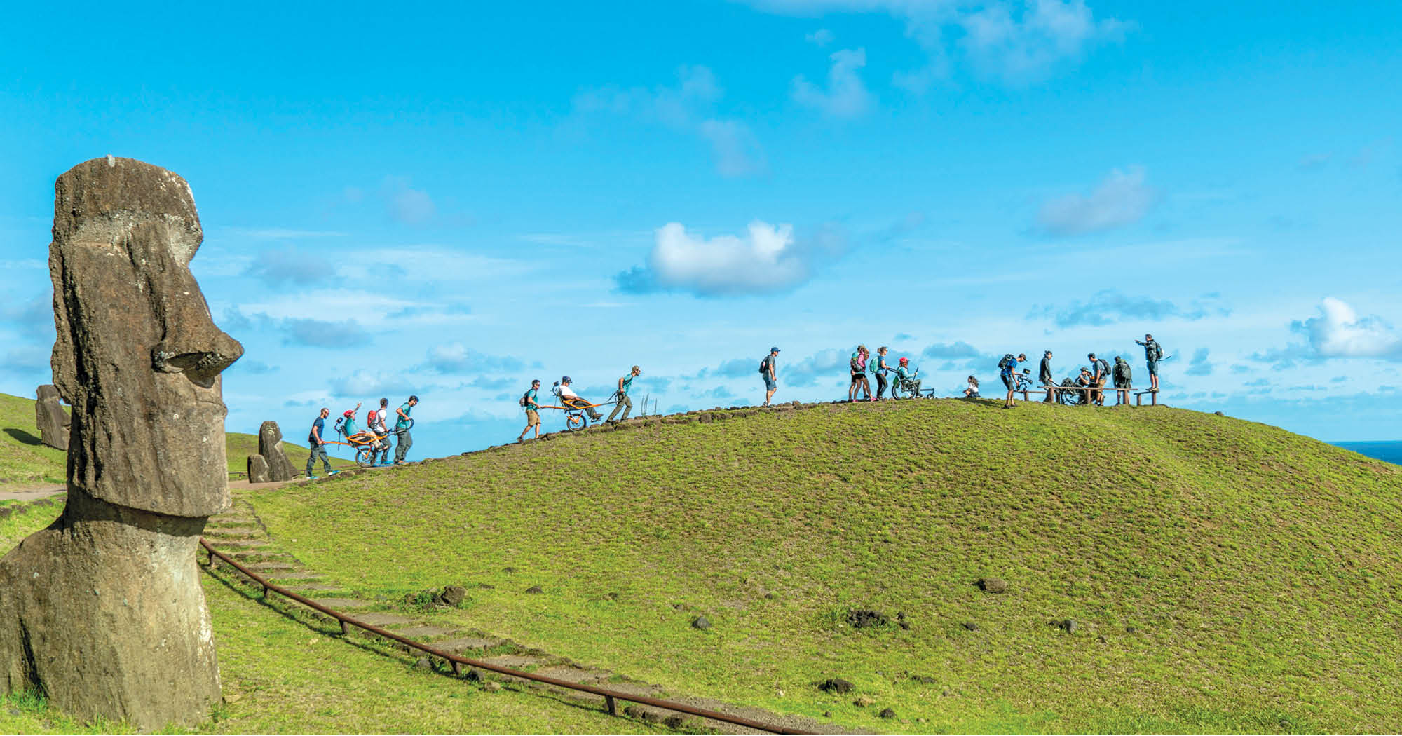 A line of people trekking through Easter Island on foot and in wheelchairs.