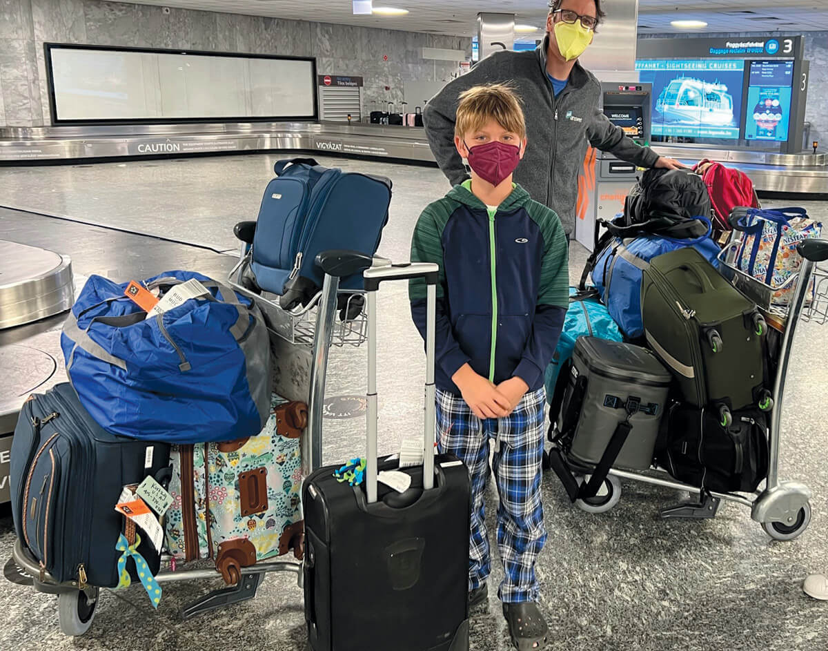 A man and a boy at an airport's baggage carousel standing with more than a dozen pieces of luggage.