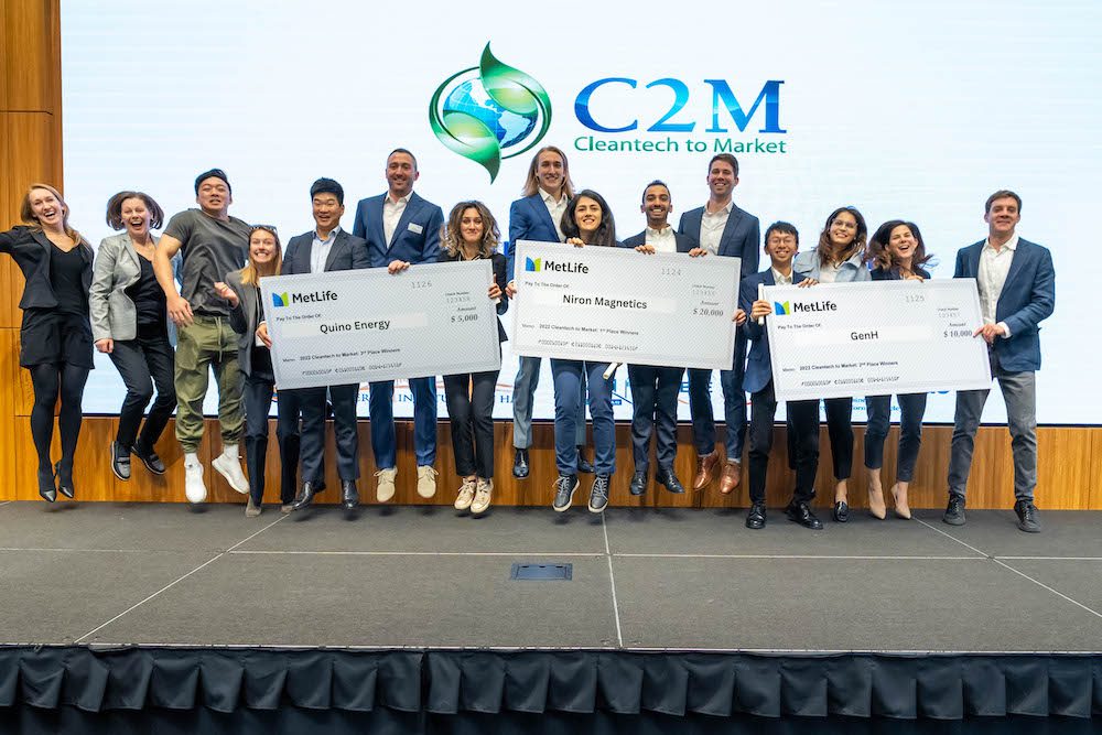students holding large checks on stage at Haas for winning at C2M summit.