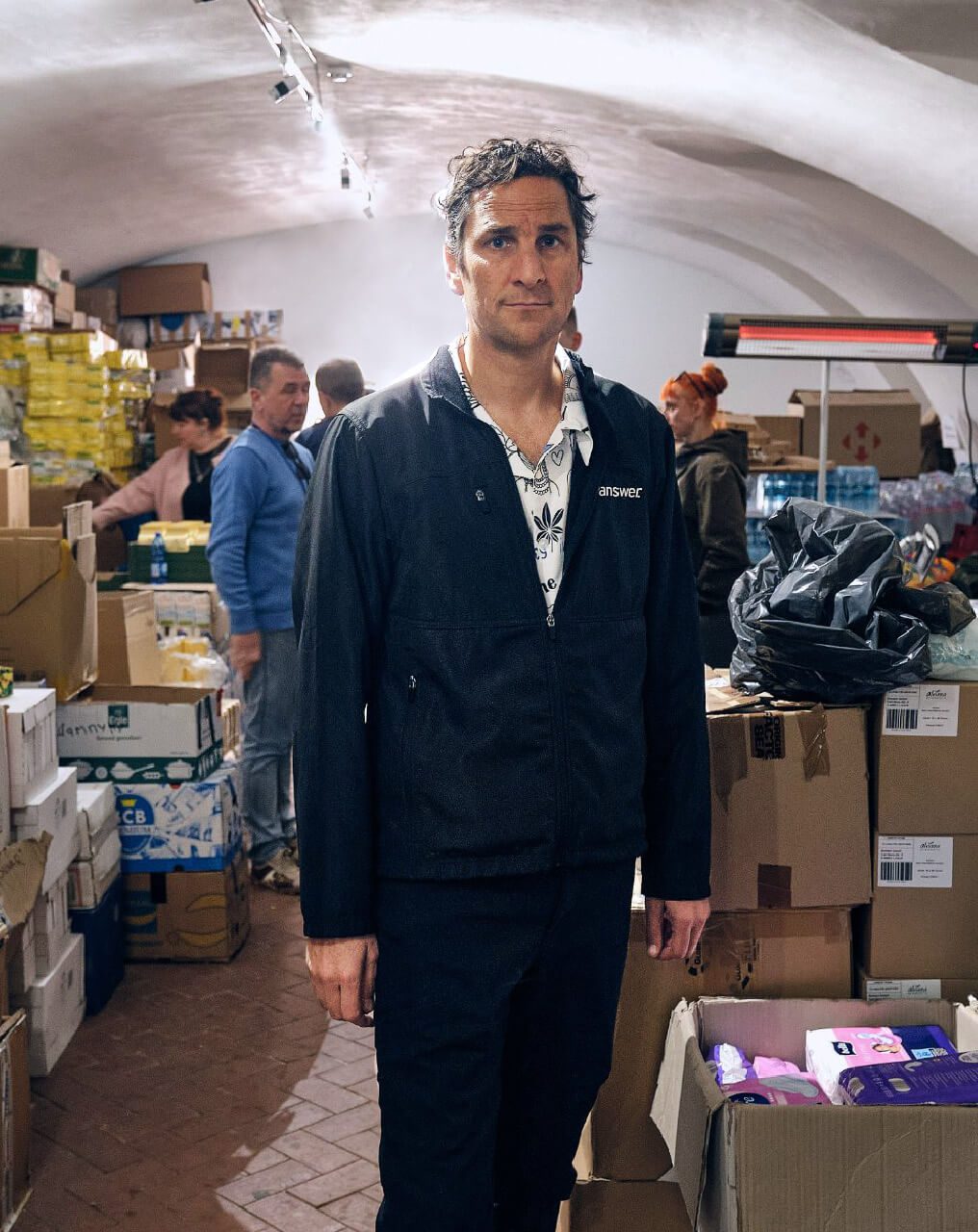 Man standing amid boxes of donations of clothes and food for Ukrainian people.