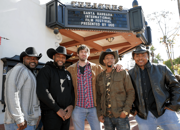 five men standing in front of a movie marquis.