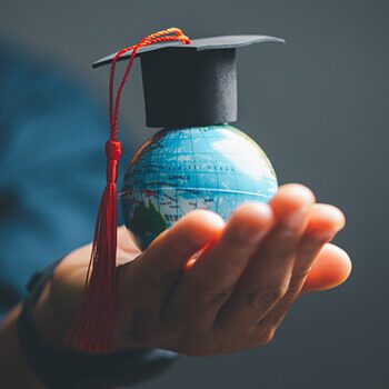 Outstretched hand holding a small globe with a graduation cap on top of it. Photo: JD8/Adobe Stock.