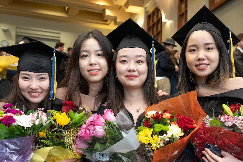 Female MFE graduates smiling while holding bouquets