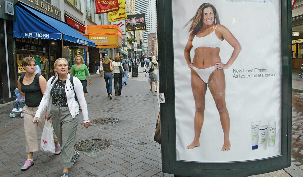 Two women walking by a Dove ad with a curvy woman on a Boston street.