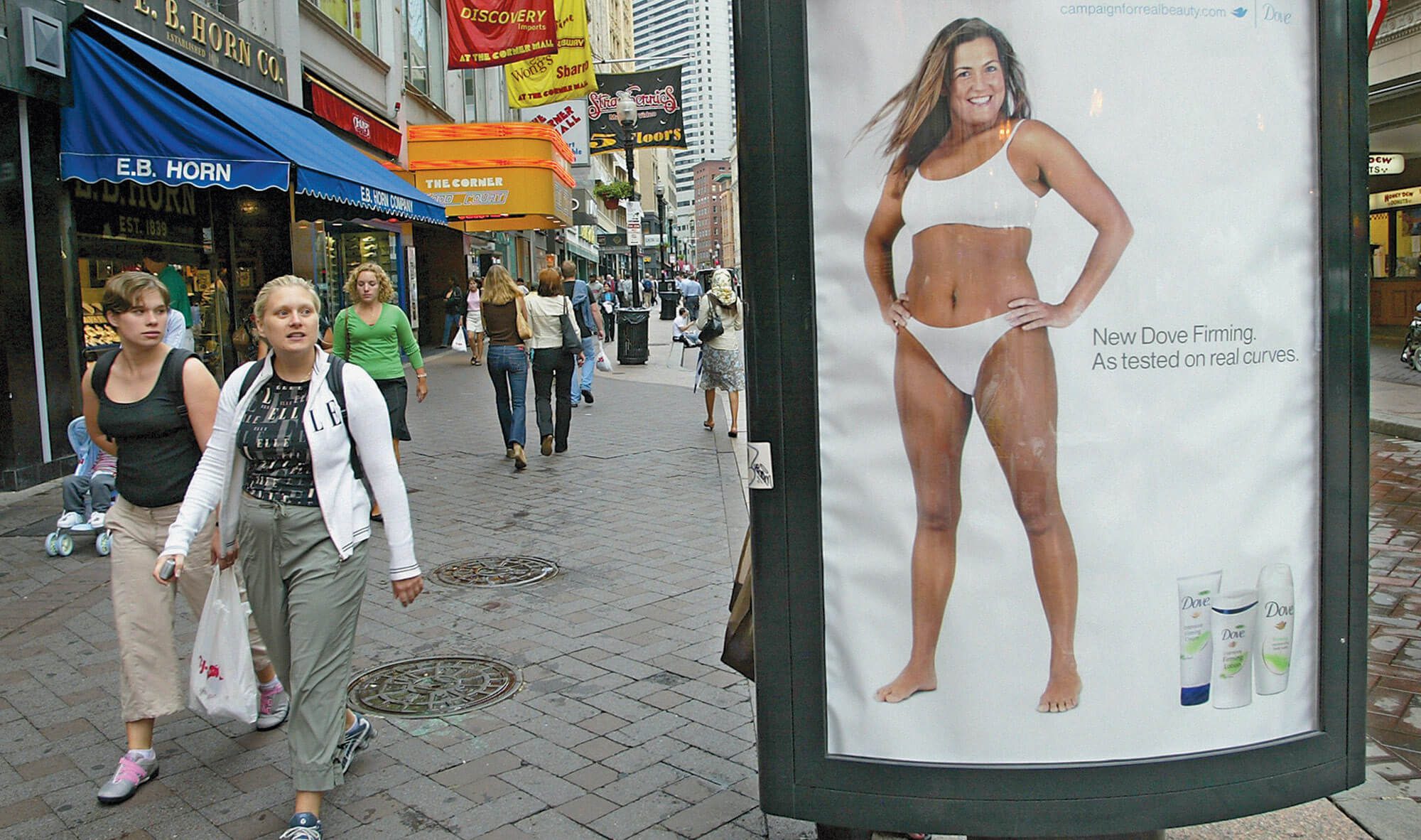 Two women walking by a Dove ad with a curvy woman on a Boston street.