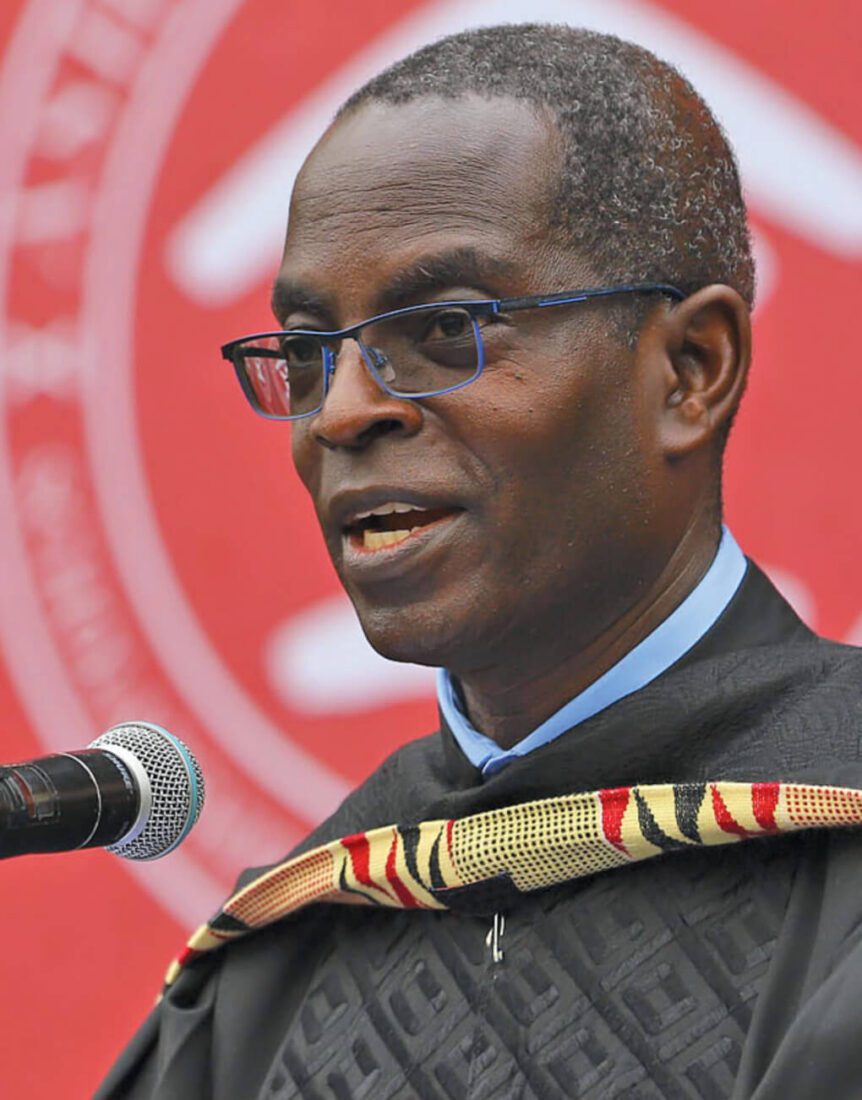 Patrick Awuah in graduation gown and hood standing in front of a microphone speaking.