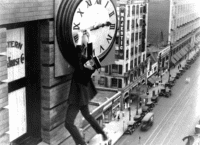 Black and white photo of man holding onto a large clocktower.