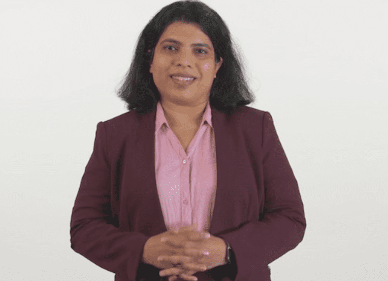 Woman smiling. Dark shoulder length hair. Maroon blazer. Pink Shirt. White backdrop.