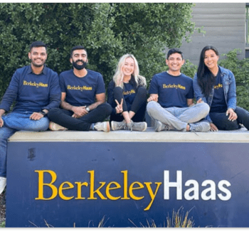 5 Haas Students sitting on Berkeley Haas sign. Smiling.
