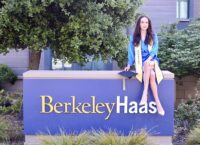 person sitting in commencement attire on Berkeley Haas sign