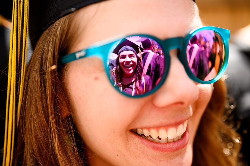Close-up of a graduate's mirrored sunglasses in which another graduate can be seen.