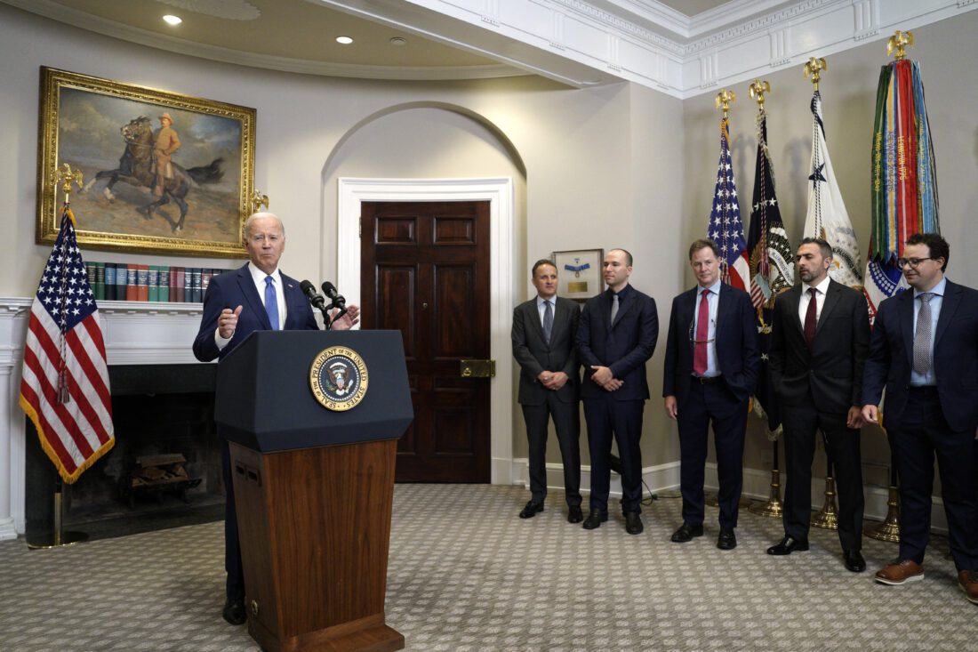 U.S. President Joe Biden stands at a podium at the White House speaking. To his right are CEOs of seven leading AI companies.