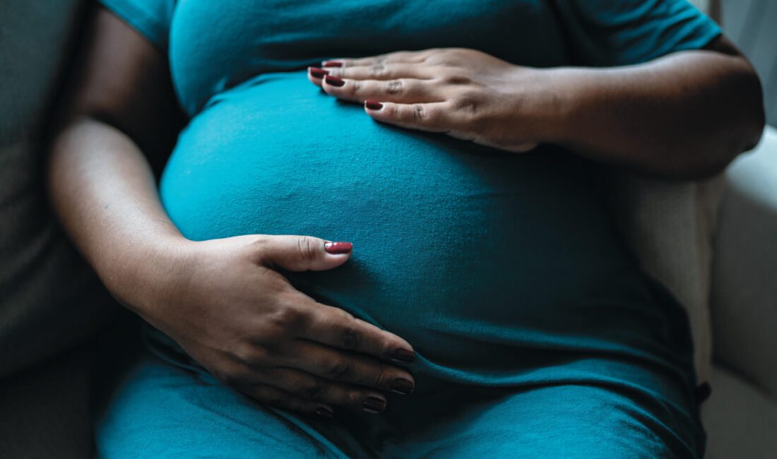 Woman with both hands on her pregnant belly.