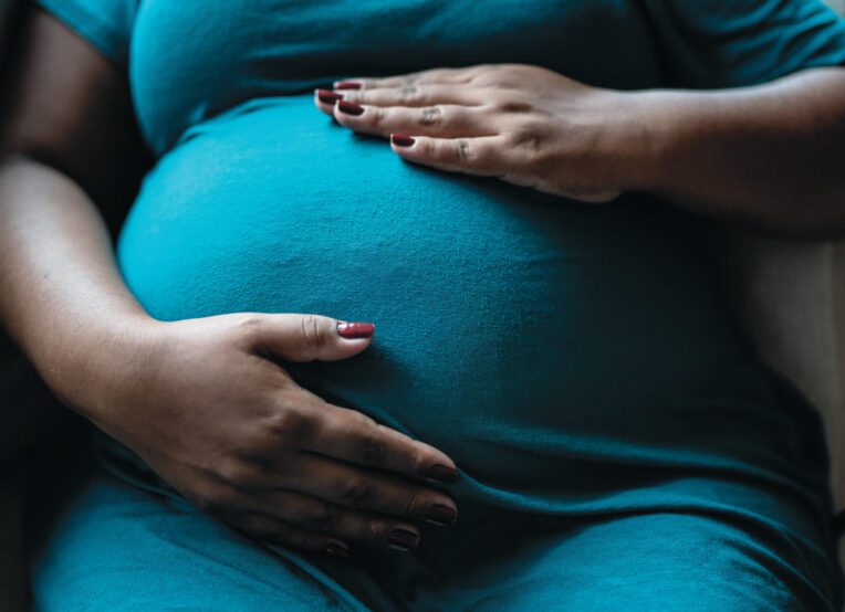Woman with both hands on her pregnant belly.