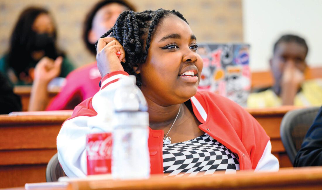 Smiling young Black woman in a red coat with a black-and-white checkered shirt.