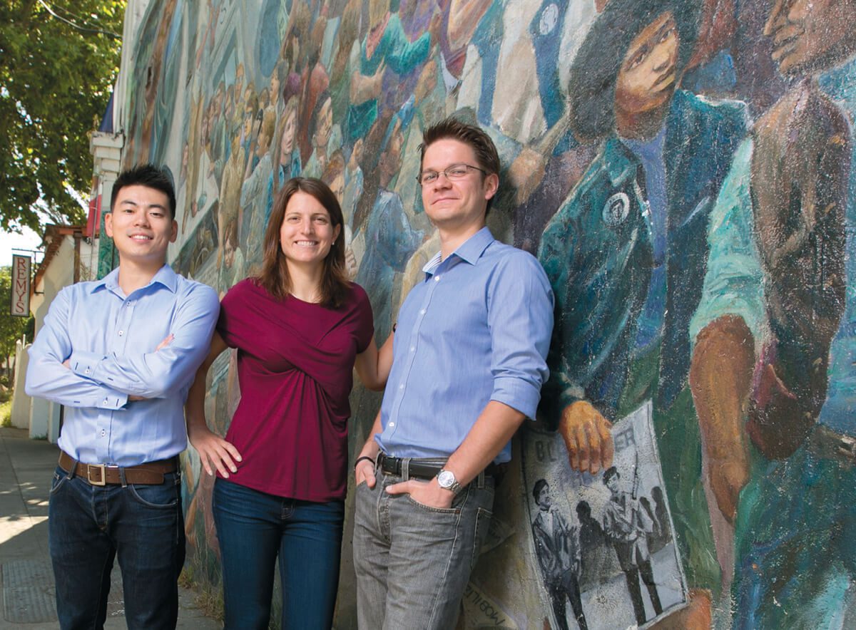 A woman flanked by two men standing in front of a mural on Telegraph Avenue in Berkeley.