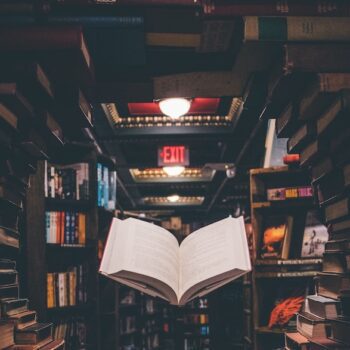 An open book floating under a light amongst a room full of books.