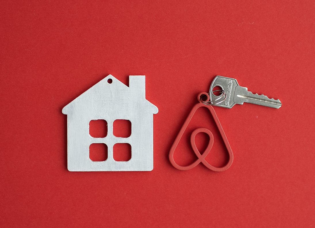 Illustration showing a key on a keychain shaped like the Airbnb logo next to a cutout paper house
