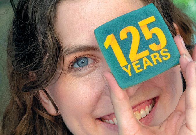Woman holding up a cookie with 125 years written on it.