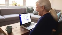 Photo of a woman with gray hair in a ponytail smiling as she looks at a laptop screen showing the Healthpilot website.