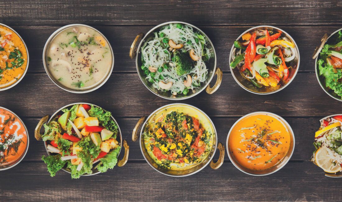 Dark wood table with lineup of multiple bowls of international cuisine.