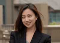 Young Asian American woman, alumna smiling in dark blazer and light top.