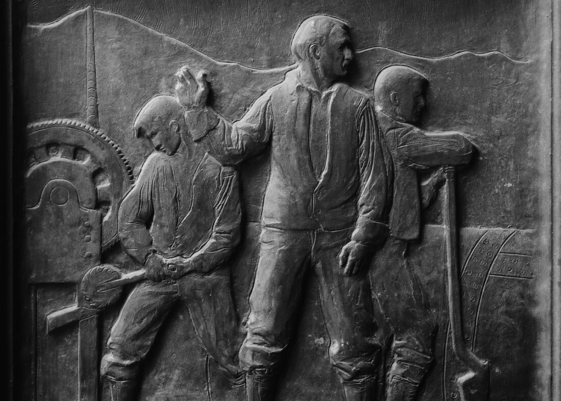 Picture of a carving of 3 men working with machinery.