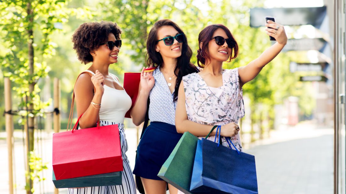 Three women with shopping bags taking a selfie in acity.