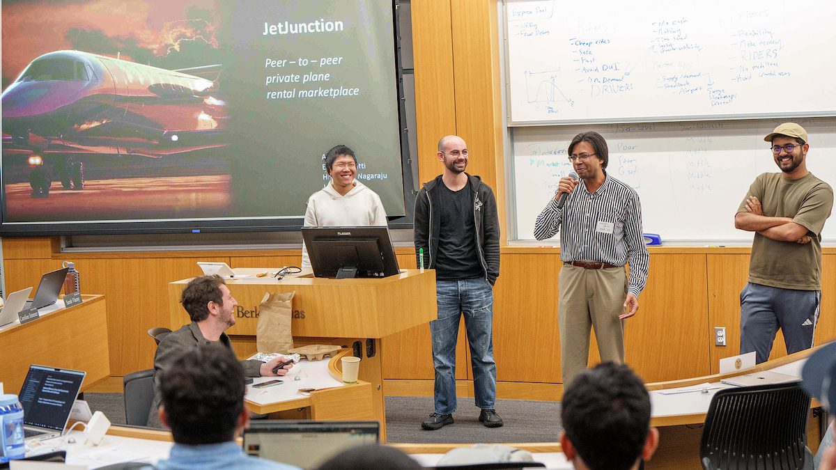 four students standing in front of a classroom pitching an idea
